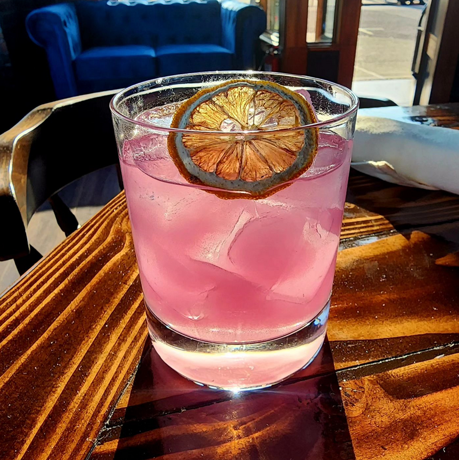 A close-up of a beautiful pink cocktail with a dried lemon slice in it.