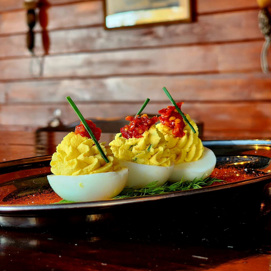 A close-up of three gorgeous deviled eggs, each bearing a single chive and a daub of red sauce.