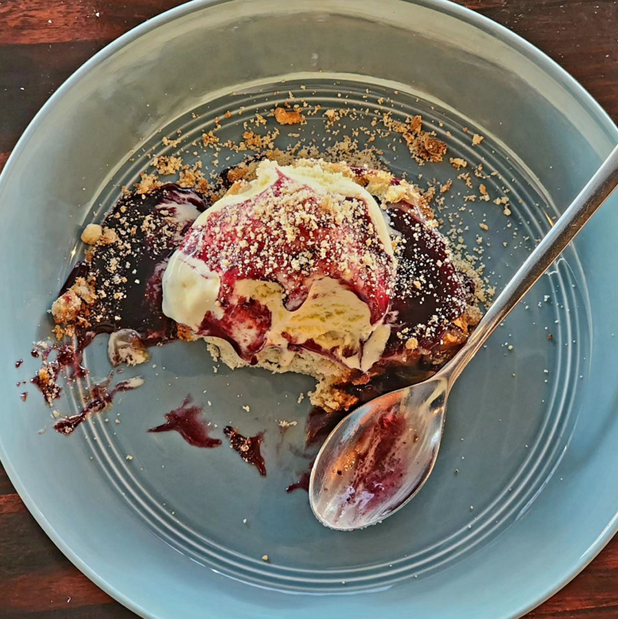 A top-down closeup of a half-devoured plate of the Admiralty's signature hog jowl ice cream, topped with red compote and some kind of crumble.